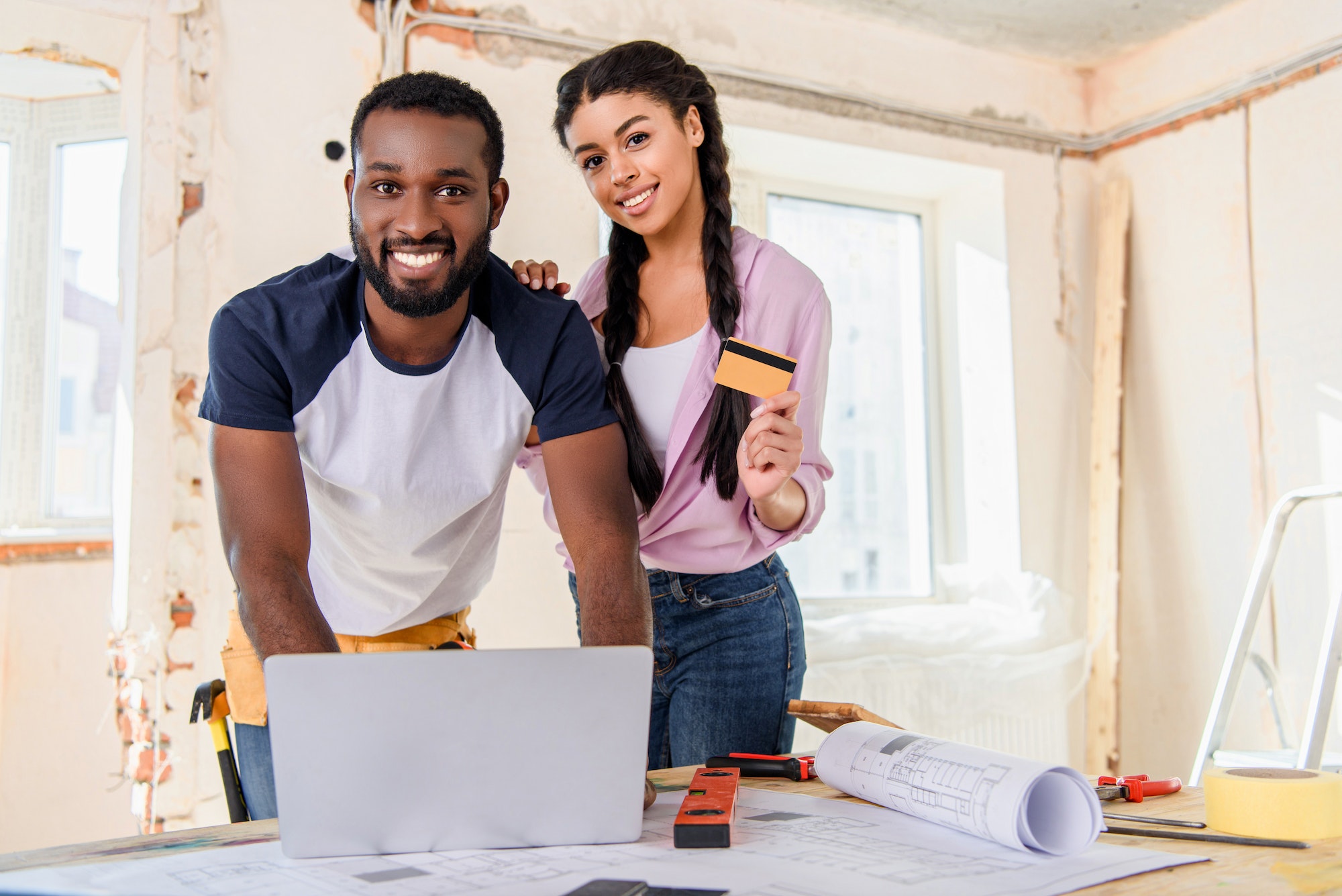 smiling young couple using laptop for e-shopping while making renovation of home